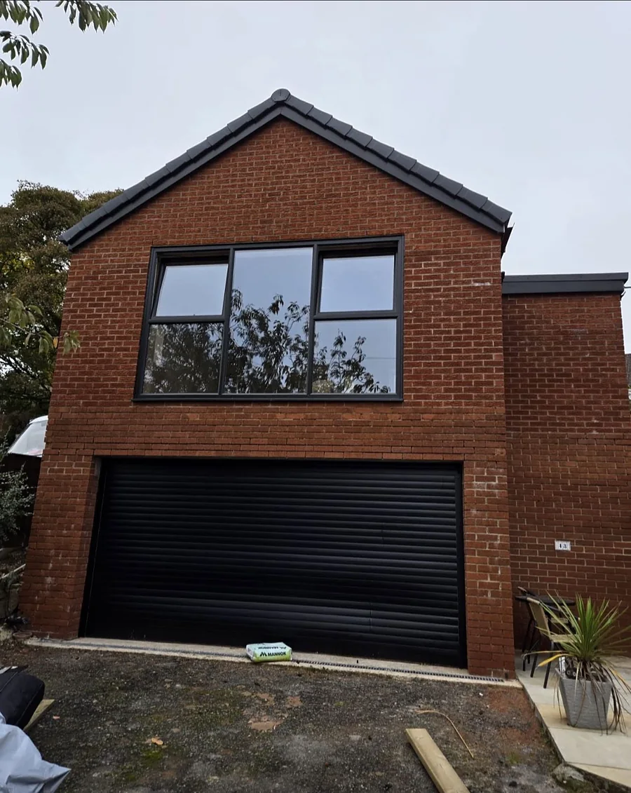 Finished brick garage extension with a black roller door and a gable window